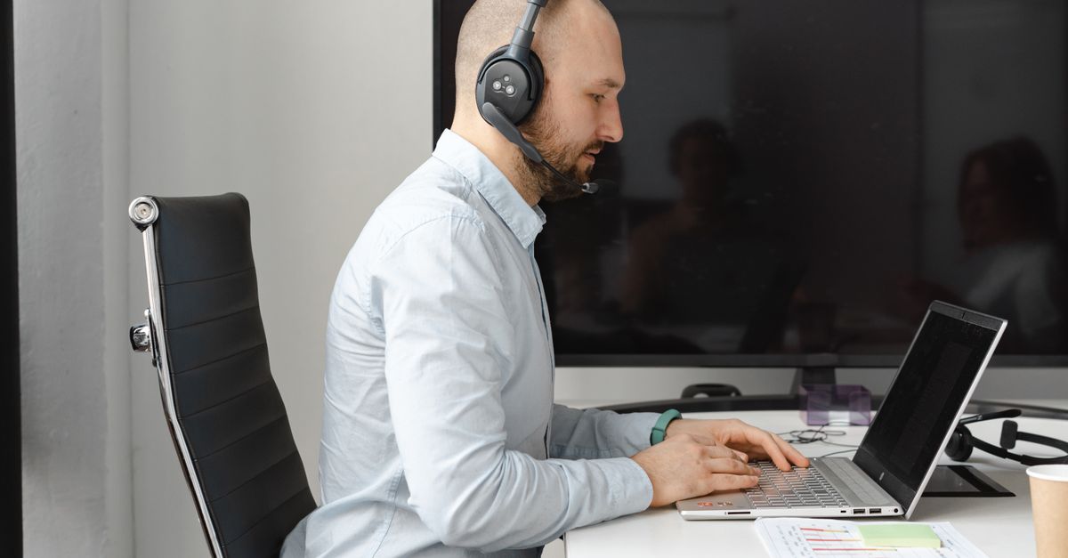 A focused call center agent with headphones working on a laptop in an office.